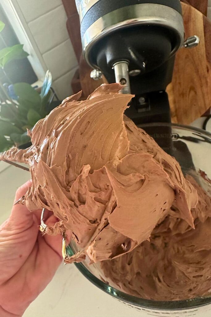 A finished batch of whipped chocolate butter that is stuck on the whisk of the mixer. It's lighter in color and fully aerated.