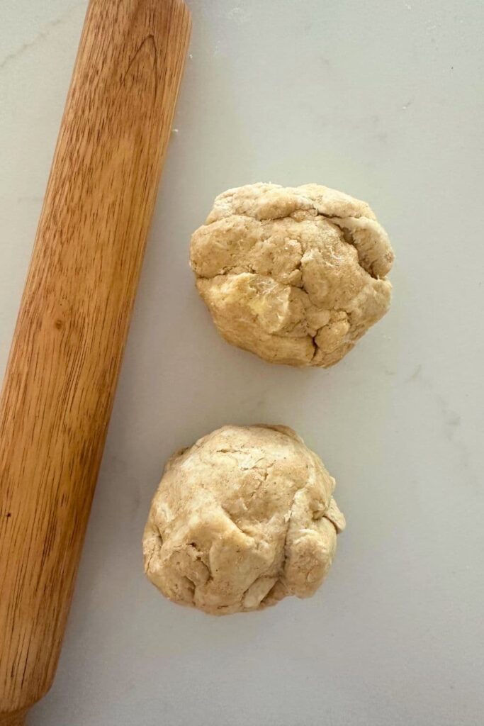 Two balls of dough sitting next to a wooden rolling pin.