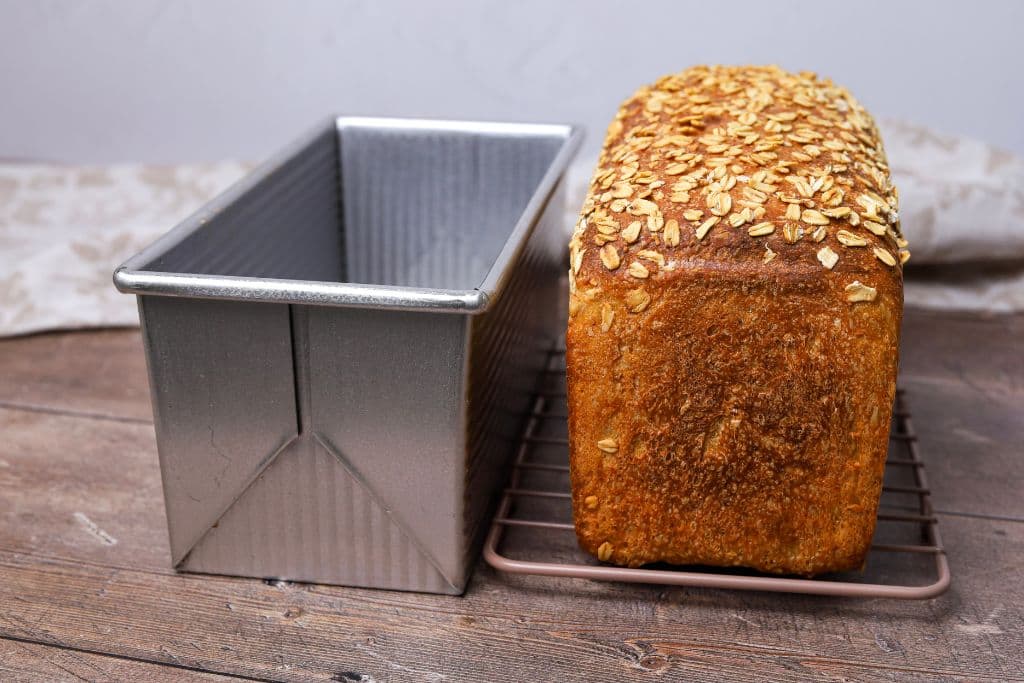 A loaf of sourdough maple oat sandwich bread that has been baked and taken out of the loaf pan. It's sitting next to the loaf pan it was baked in.