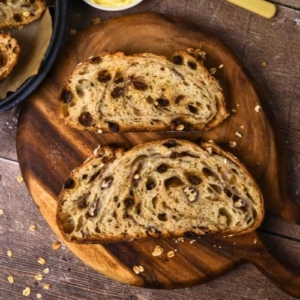 2 slices of sourdough apple crisp loaf set out on a round wooden board.