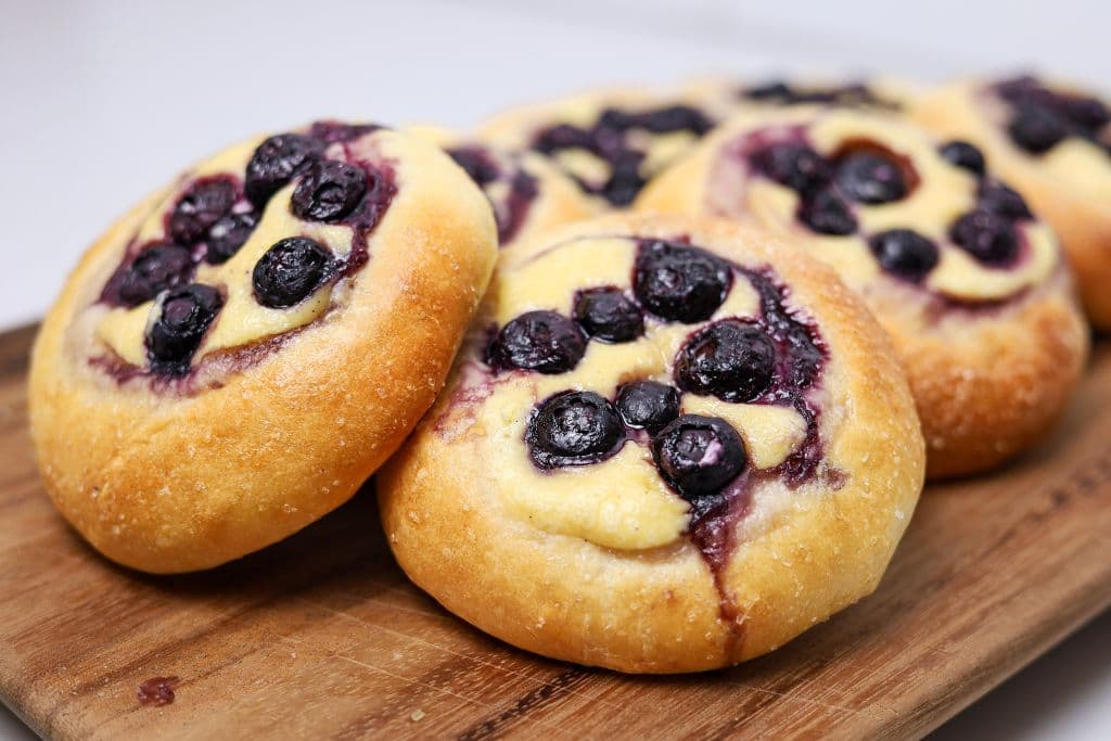 A pile of sourdough blueberry brioche tarts filled with vanilla cheesecake filling.