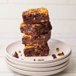 A stack of sourdough peanut butter brownies sitting on 4 white plates. The brownies are stacked haphazardly so you can see all the angles.