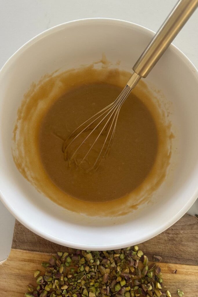 A bowl wet ingredients necessary to make sourdough honey pistachio cookies. The ingredients have been whisked together and look like runny caramel.