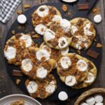 Recipe feature image for S'mores Sourdough Cookies. There are 7 cookies photographed from above. They are sitting on a round, black serving platter.