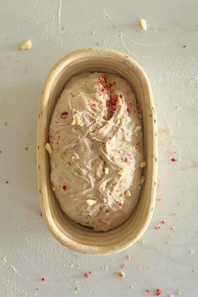 A sourdough strawberries and cream loaf that has been shaped and placed into an oval shaped banneton.