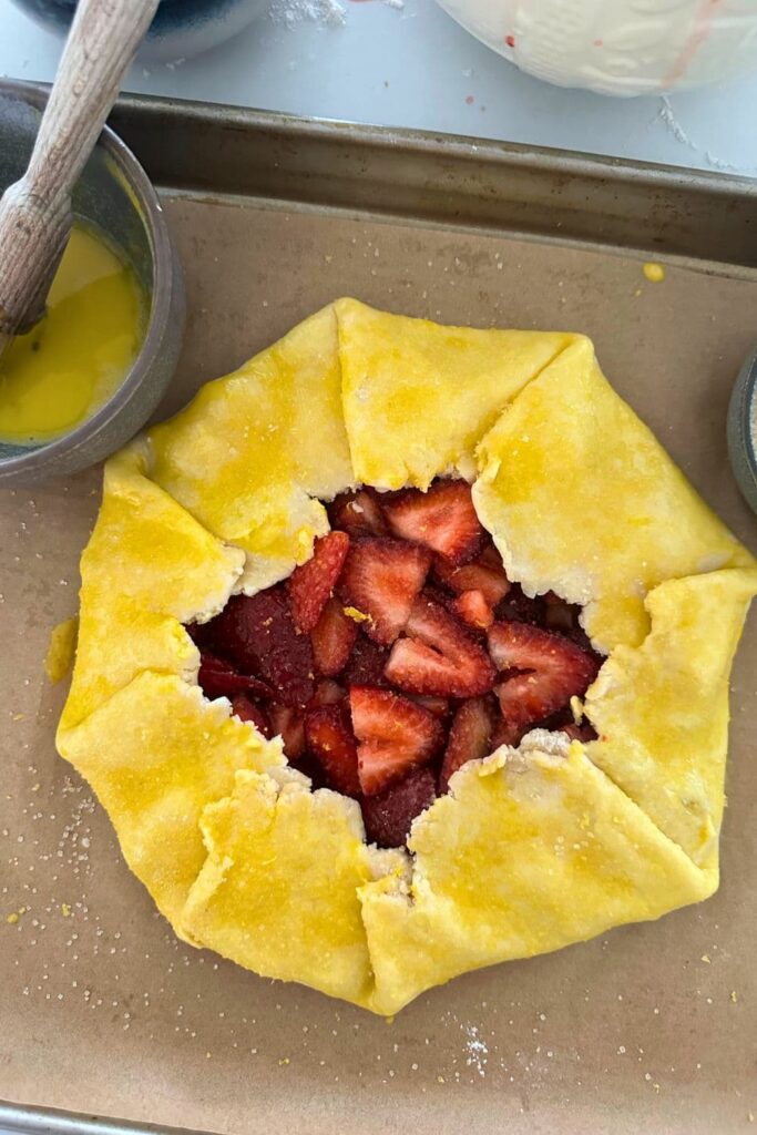 Sourdough strawberry galette that has been folded up and egg washed, as well as sprinkled with granulated sugar. The egg yolk is very yellow because it's from a backyard chicken.