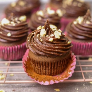 A close up photo of a sourdough chocolate cupcake topped with chocolate frosting and sprinkled with toasted hazelnuts.