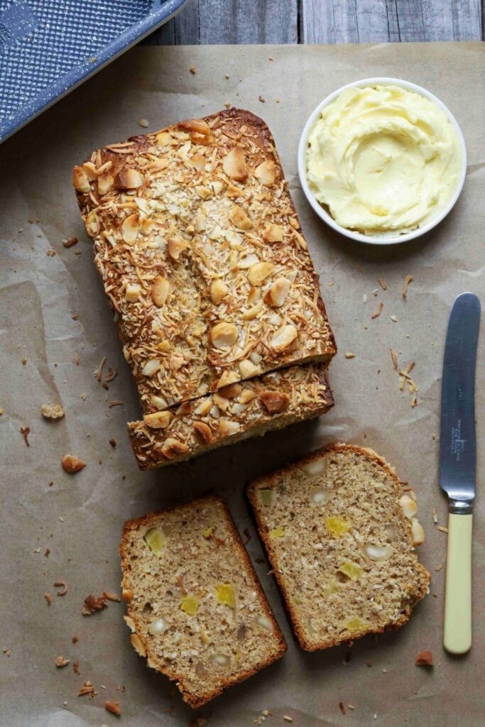 Sourdough Hawaiian banana bread on parchment paper with half the loaf sliced next to a knife and small bowl of butter.