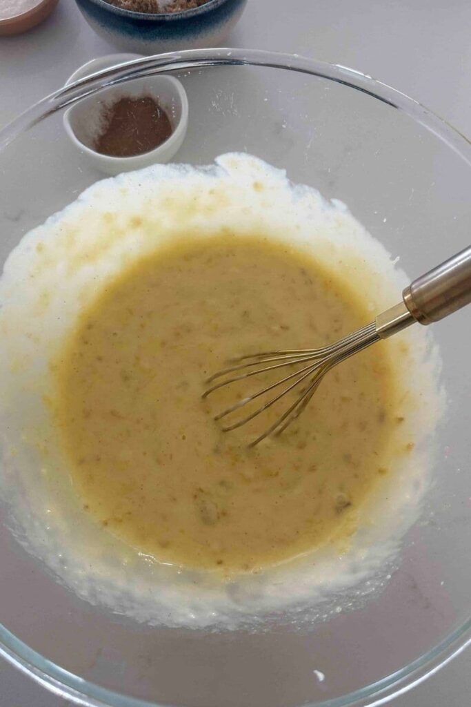 Mashed bananas with vanilla, melted butter, sourdough starter and an egg mixed in a glass bowl to make sourdough Hawaiian banana bread.