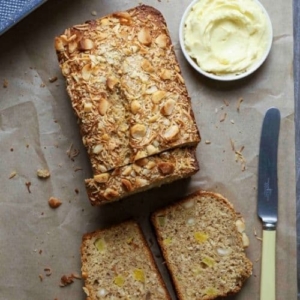 Sourdough Hawaiian banana bread on parchment paper with three slices cut next to a small bowl of butter and a butter knife.