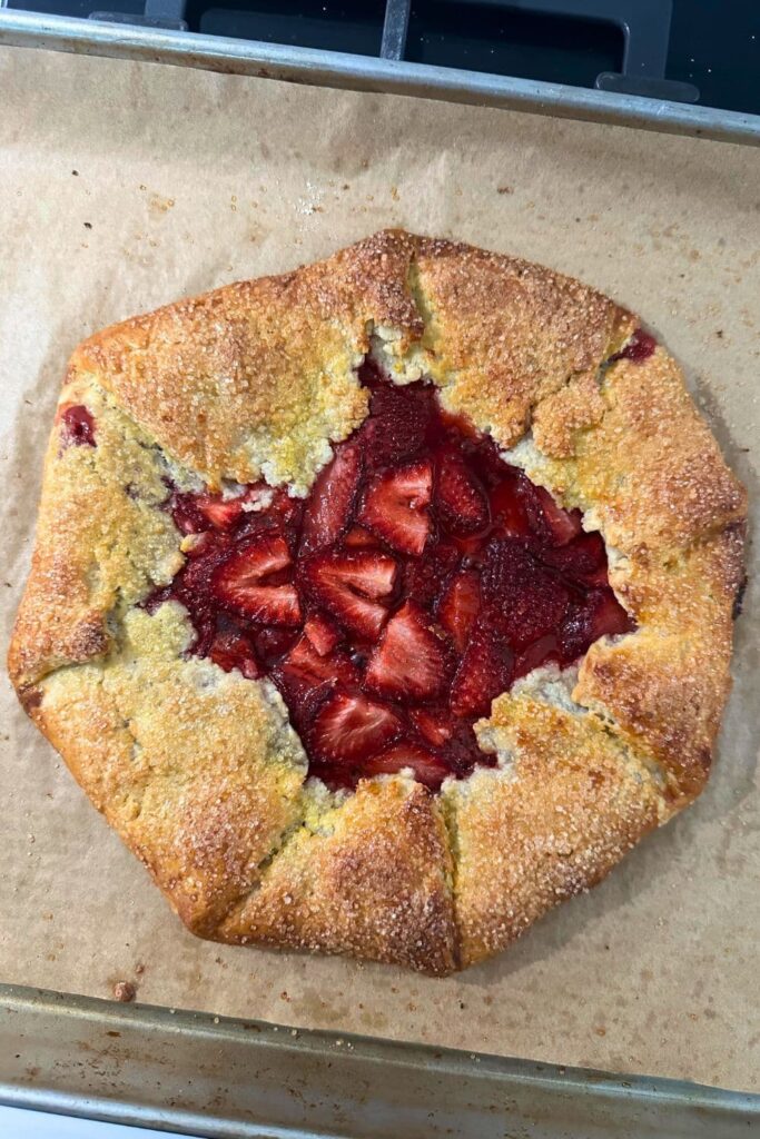 A sourdough discard strawberry galette that has just been baked and removed from the oven. The pastry is golden brown and the strawberries in the centre are red and jammy.
