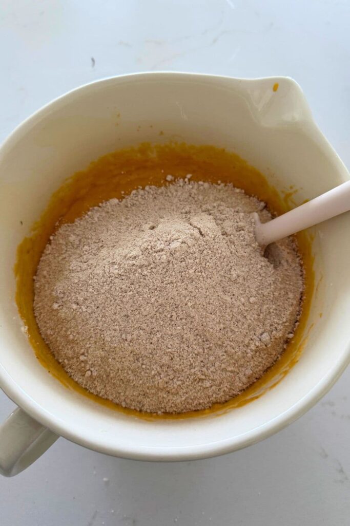 Adding the dry ingredients to the wet ingredients in a cream colored batter jug.