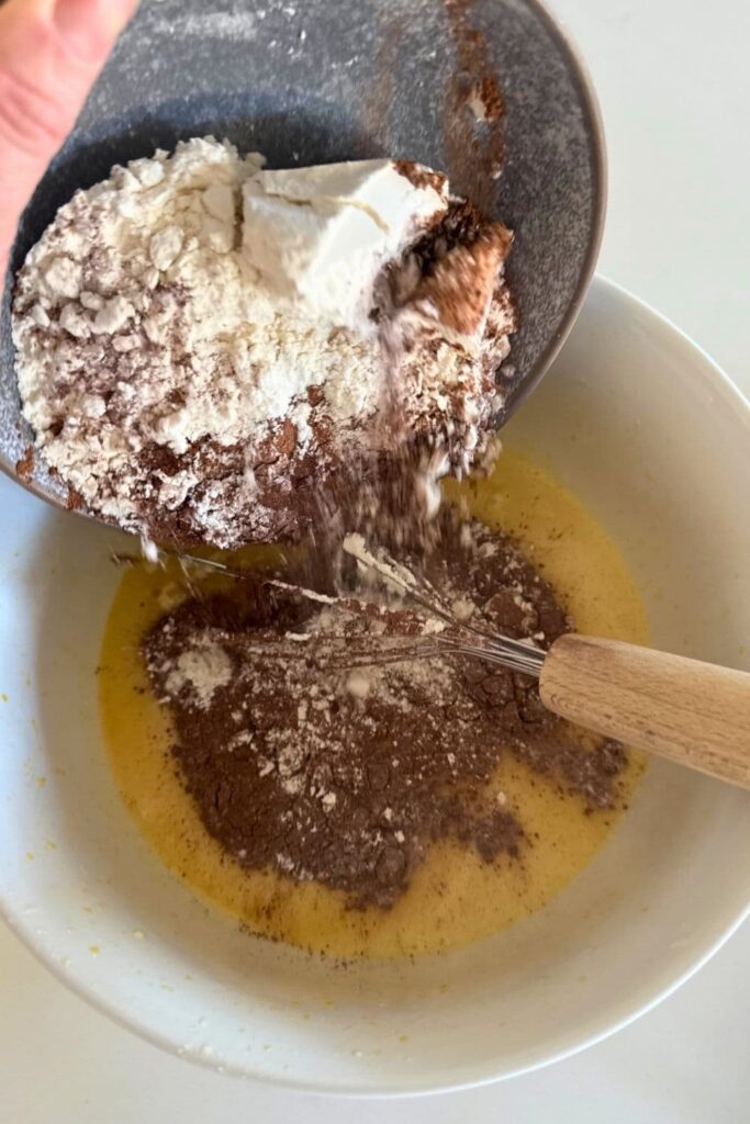 sourdough chocolate cupcake batter being made by adding dry ingredients into bowl with wet ingredients.