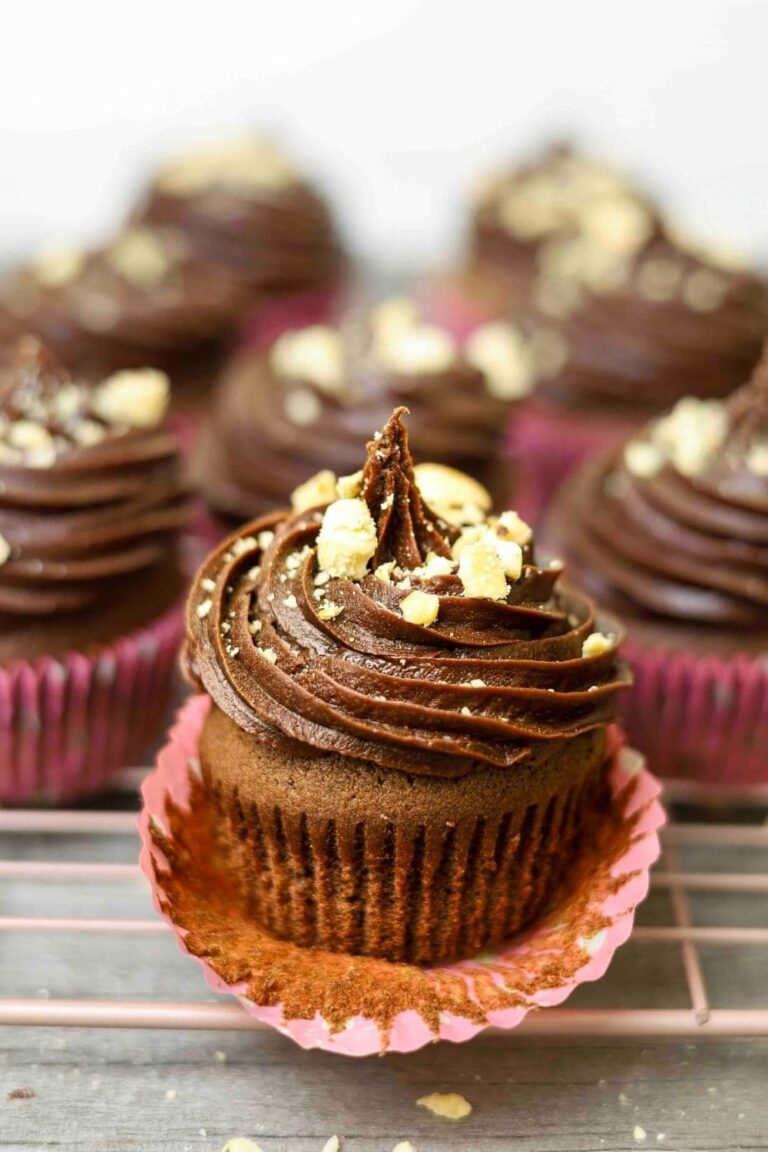 Close up of sourdough chocolate cupcake with buttercream frosting on top and paper cup slightly peeled away.