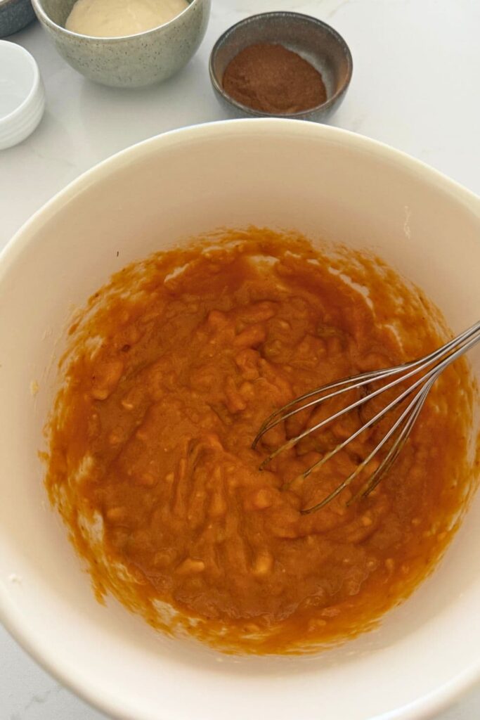 A mixing bowl containing mashed banana, eggs and pumpkin puree whisked together.