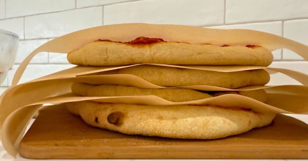 A stack of par-baked sourdough pizza crusts that have been layered between pieces of parchment paper.
