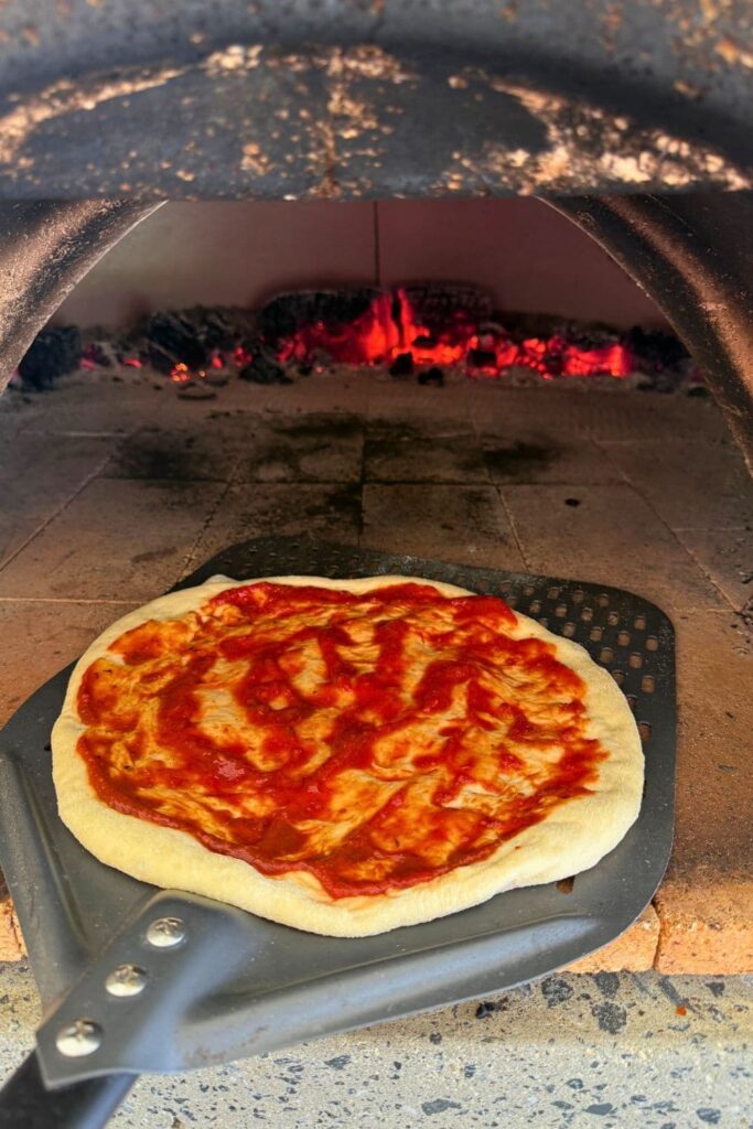 A sourdough pizza base with tomato pizza sauce on it being par baked in a wood fired pizza oven.