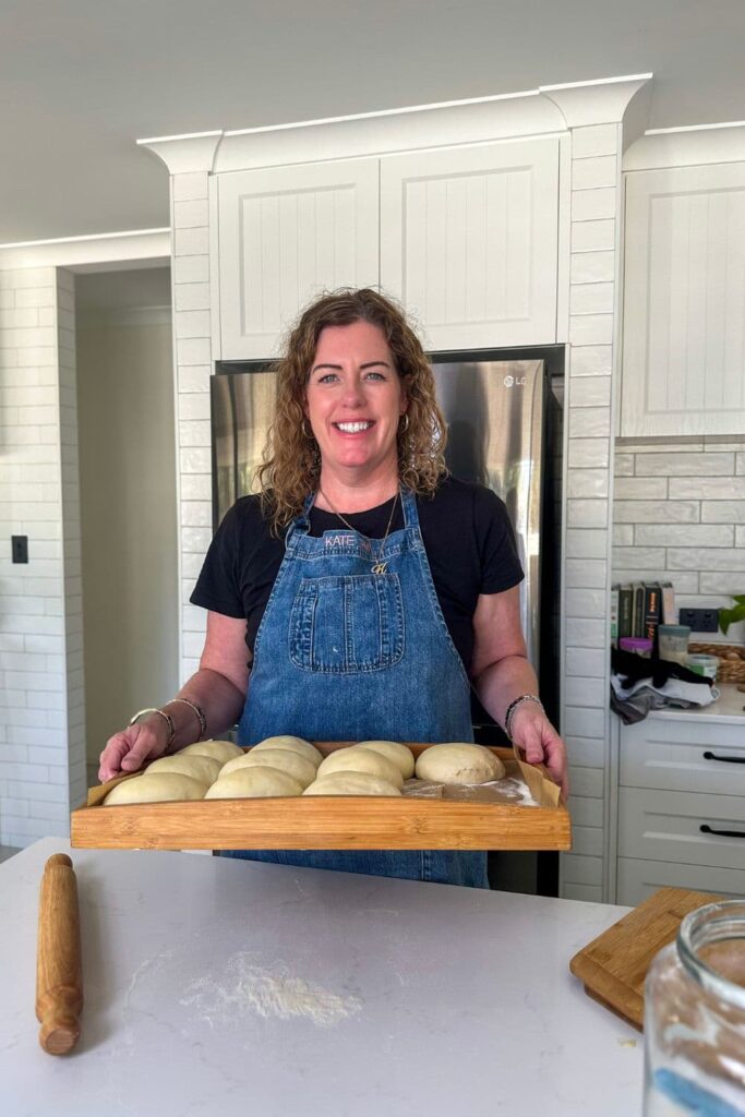 Kate from The Pantry Mama standing in her kitchen holding a tray of sourdough pizza dough balls.