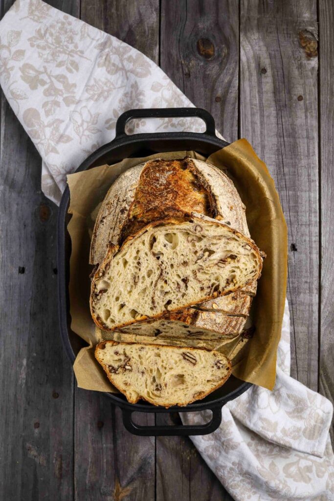 Sourdough maple pecan loaf sliced inside of parchment paper lined baking dish to show inside of bread.