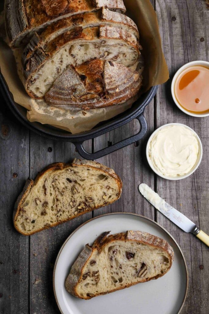 Sourdough maple pecan loaf sliced and placed on plate near butter and knife.