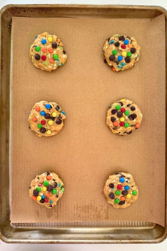 Sourdough monster cookie dough in cookie shape on parchment paper lined baking sheet.