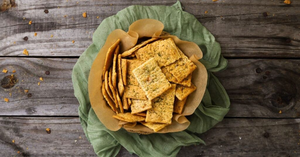 Sourdough ranch crackers displayed in a small basket surrounded with a green napkin displayed on a rustic wooden board.