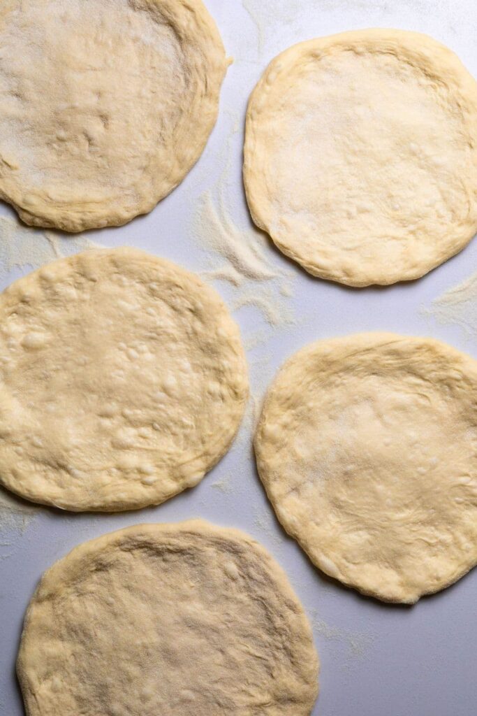 5 sourdough pizza bases laid out on the counter ready to be frozen.