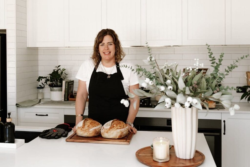 Photo of Kate Freebairn from The Pantry Mama standing behind her kitchen counter with 2 loaves of sourdough bread in front of her.