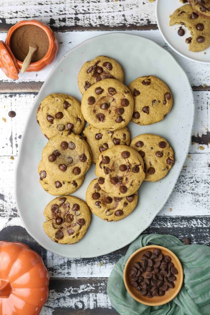 Sourdough pumpkin chocolate chip cookies on a serving plate next to a bowl of chocolate chips and spices.