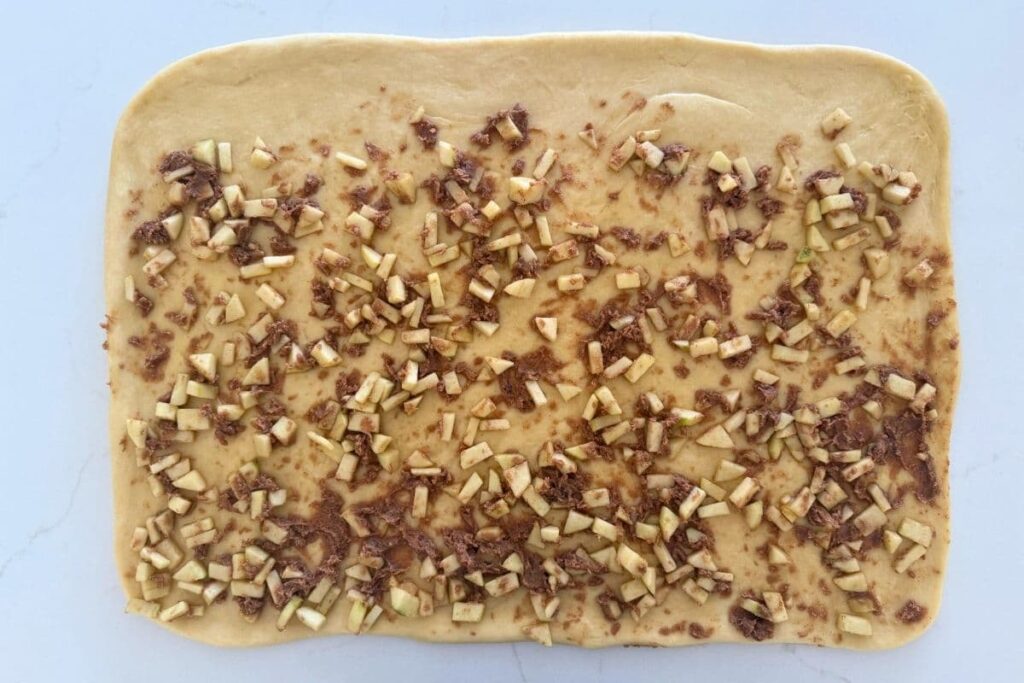 Adding filling to rolled out dough for sourdough apple cinnamon rolls.