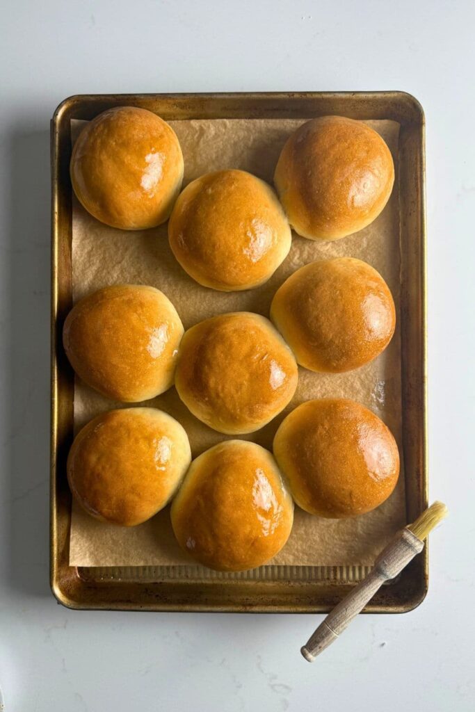 Sourdough burger buns fresh baked on baking sheet lined with parchment paper.