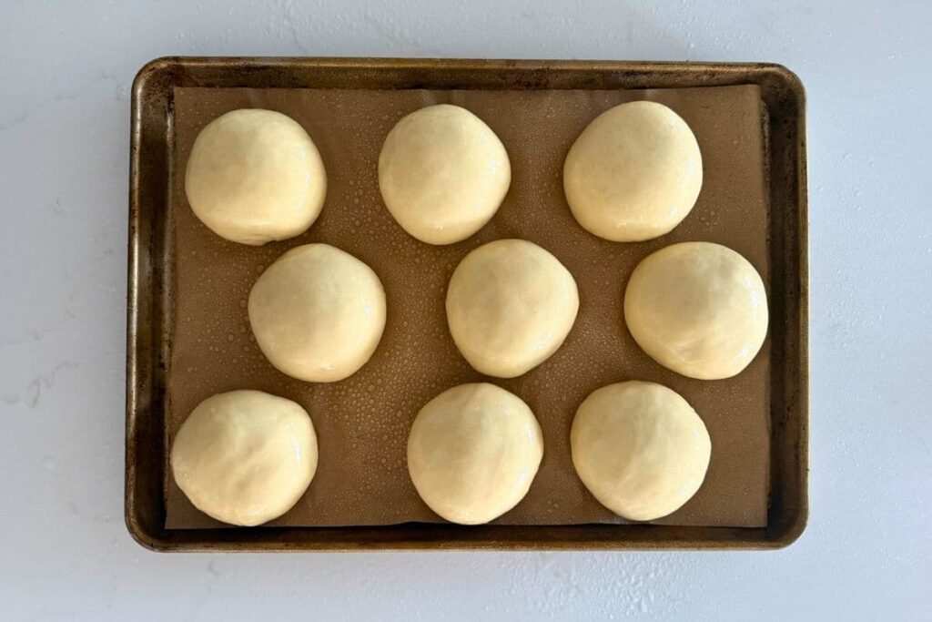 Sourdough burger bun dough balls on baking sheet after second rise.