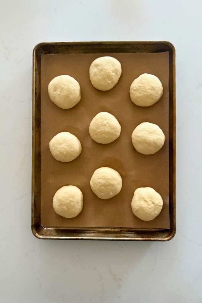 Sourdough burger bun dough balls on parchment lined baking sheet ready for second rise.