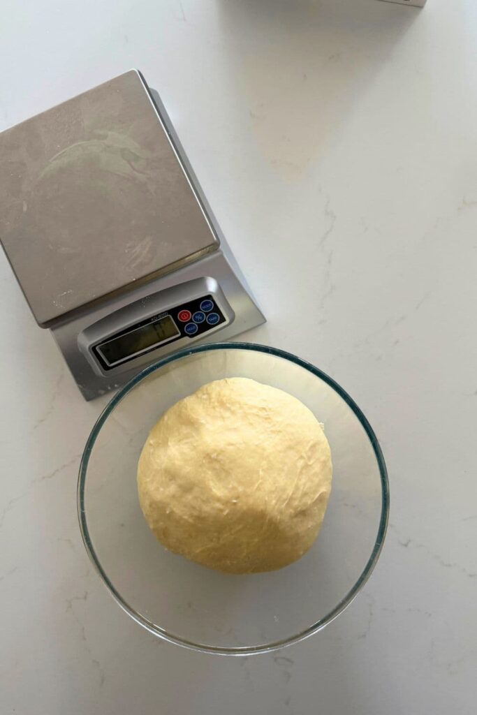 Sourdough burger bun dough after first rise sitting next to kitchen scale.