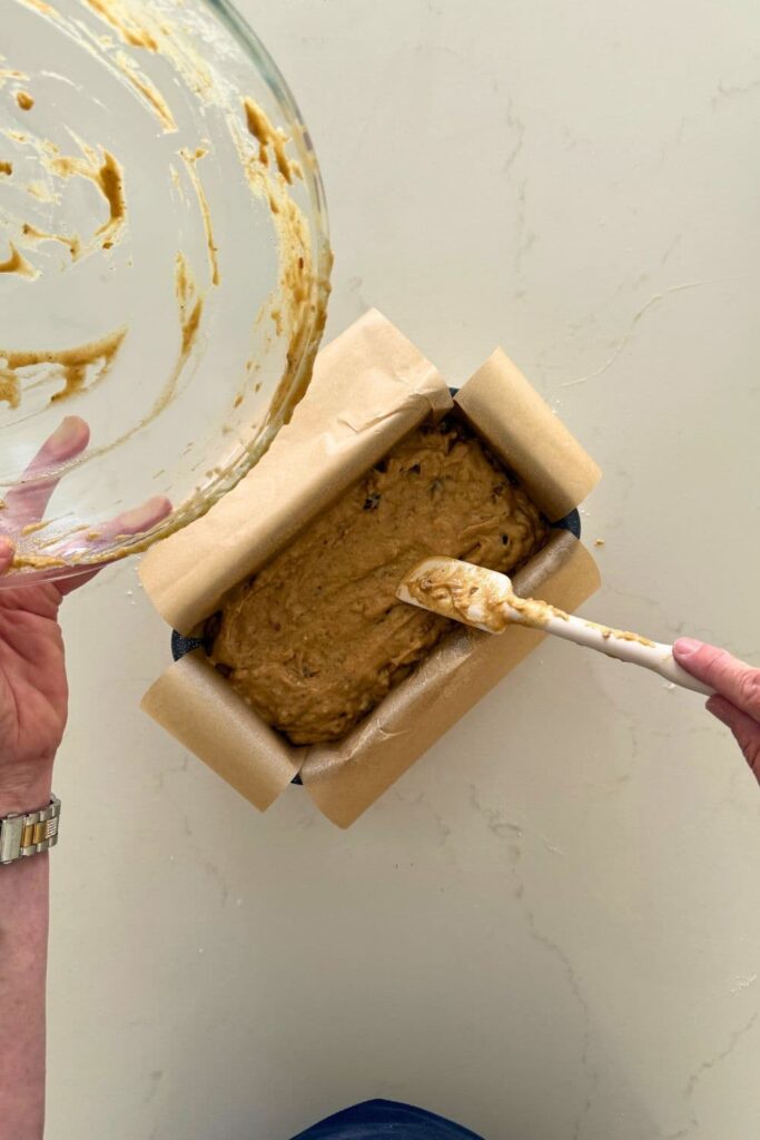 Adding batter to loaf pan to make sourdough date and walnut loaf cake.
