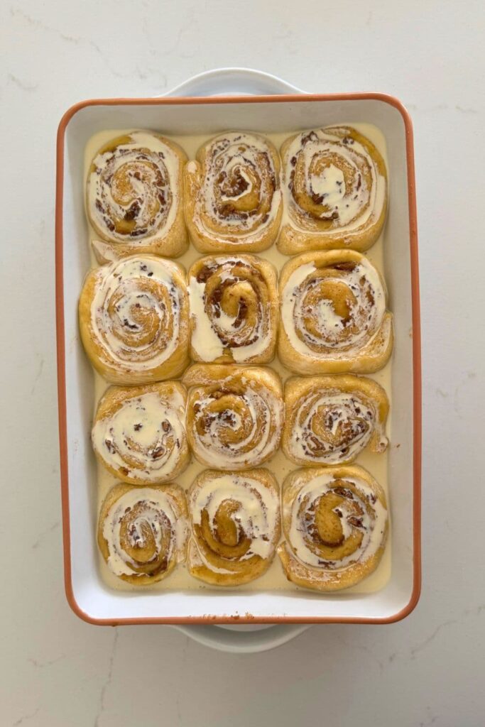 Sourdough maple pecan roll dough sliced in baking dish with heavy cream poured on top and soaked in.