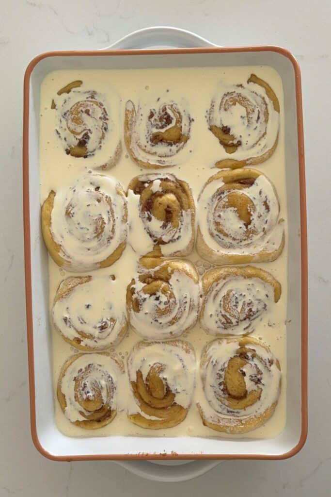 Sourdough maple pecan roll dough sliced in baking dish with heavy cream poured on top.