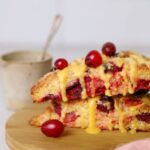 Close up of two sourdough orange and cranberry scones stacked on a wooden plate.