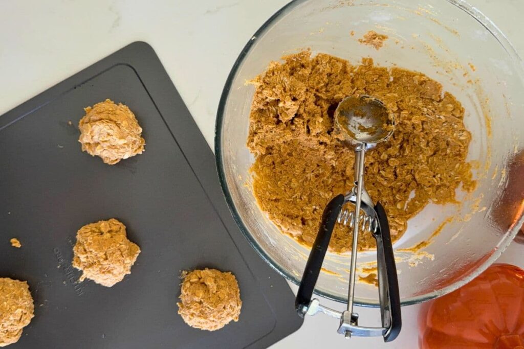 Sourdough pumpkin oatmeal cookie dough in bowl being scooped onto cookie sheet with a cookie scoop.