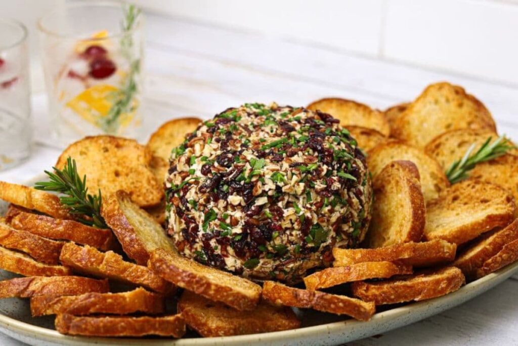 A shallow bowl of sourdough crostini with a cranberry pecan cheese ball in the center.