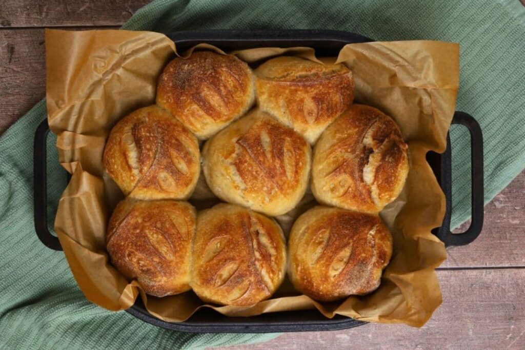 Crusty sourdough bread rolls on parchment paper in a baking dish.