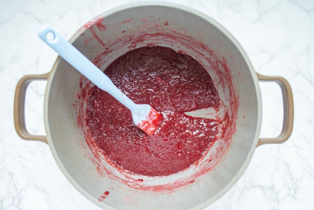 A large handled pot containing strawberry jam. The photo depicts the process of checking whether the jam is done by using a spatula in the base of the pan.