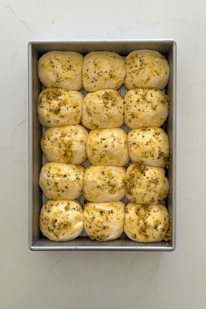 Sourdough cheese and garlic roll dough after proofing in baking dish and brushed with garlic butter.