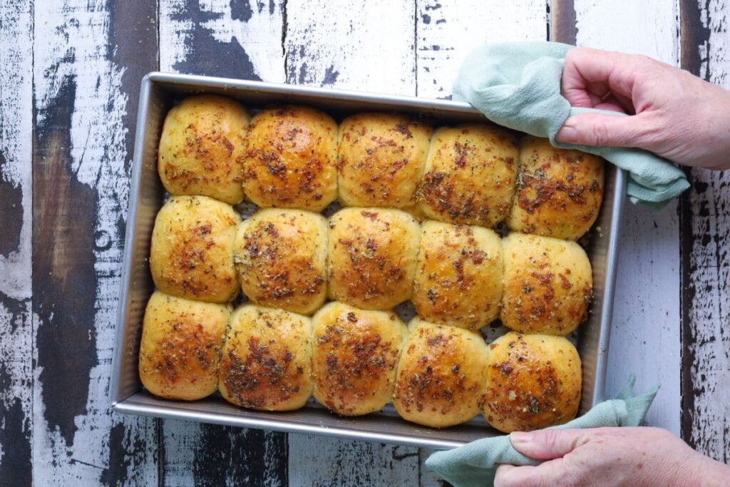 Fresh baked sourdough cheese and garlic rolls in baking pan over a wood table.