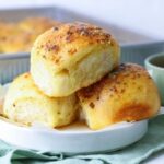 Close up of three sourdough cheese and garlic rolls on a small plate.