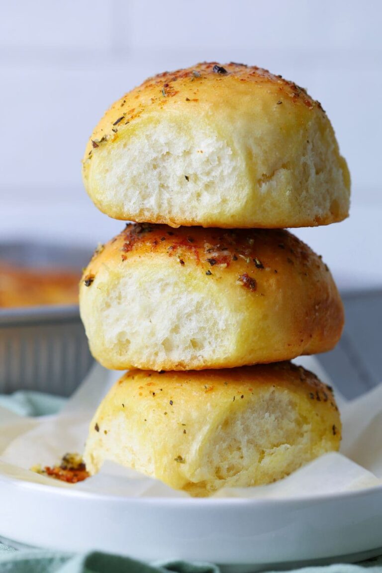 Three sourdough cheese and garlic rolls stacked on plate.