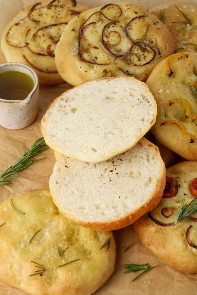Sourdough focaccia roll cut in half on a tray of sourdough focaccia rolls to show soft, pillowy inside texture.