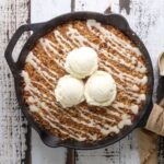 Sourdough oatmeal pumpkin cookie skillet on a wood table with three scoops of vanilla ice cream on top.