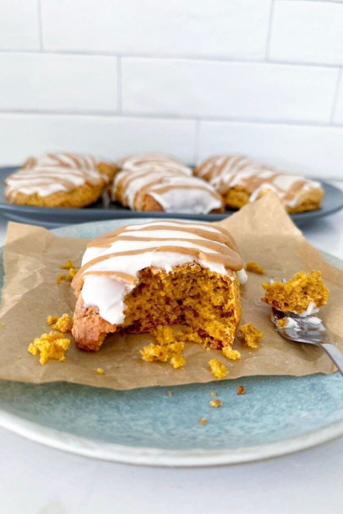 A sourdough pumpkin scone that has been cut into with a fork showing the inside crumb. They have been glazed with two types of glaze.