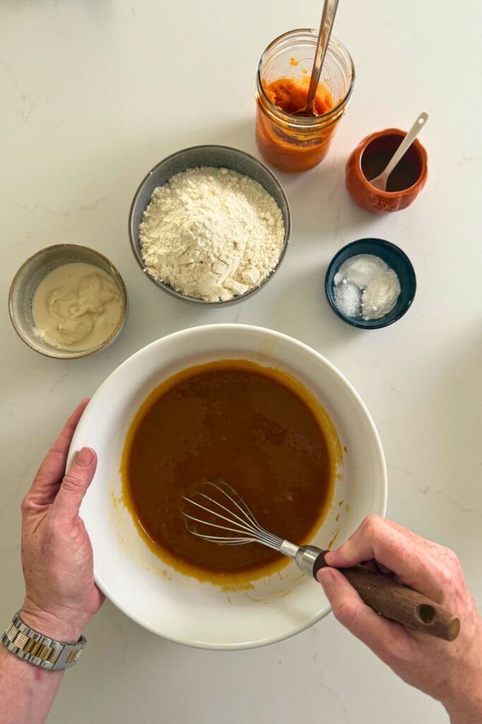 Hand whisking together wet ingredients to make sourdough pumpkin snickerdoodle cookies.